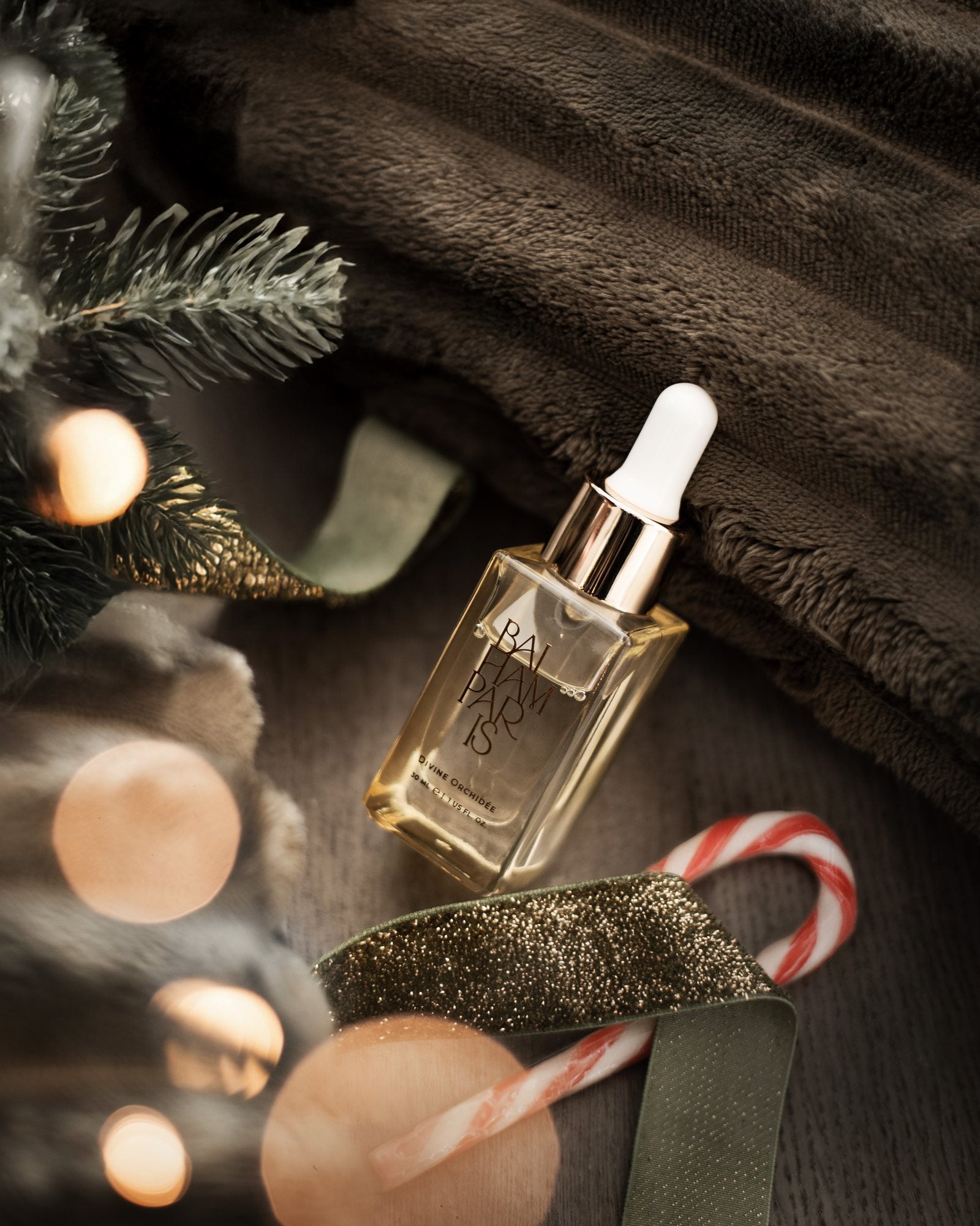 Élixir de parfum d'intérieur Baiham Paris posé parmi des branches de sapin